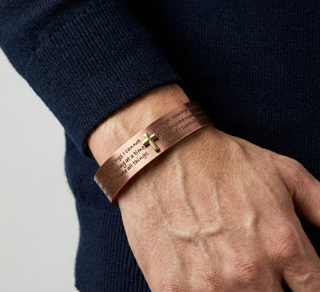 Person wearing a copper bracelet with engraved text on a plain background