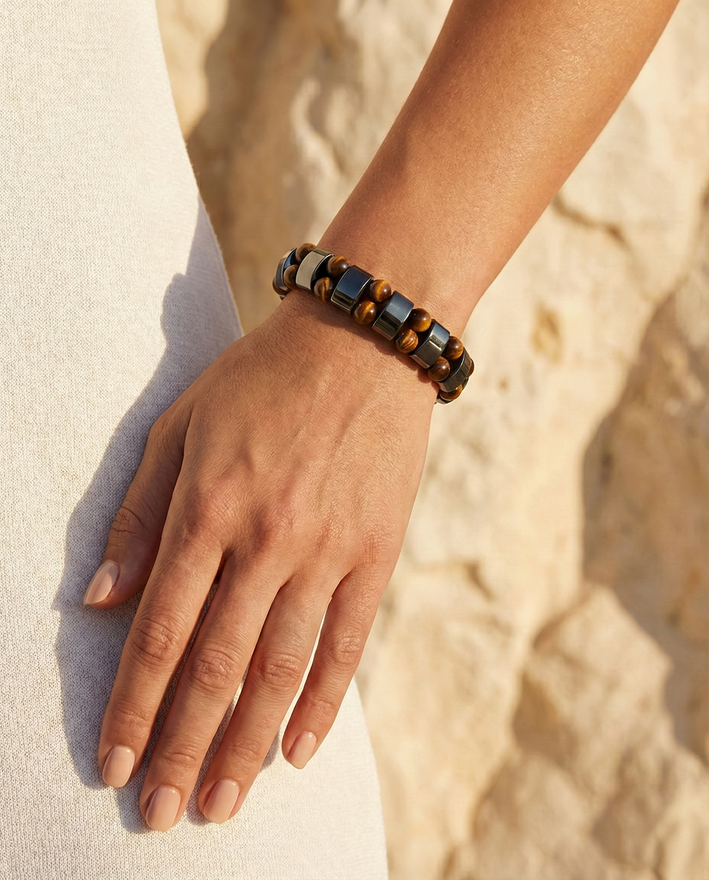 Hand wearing a beaded bracelet on a sandy background