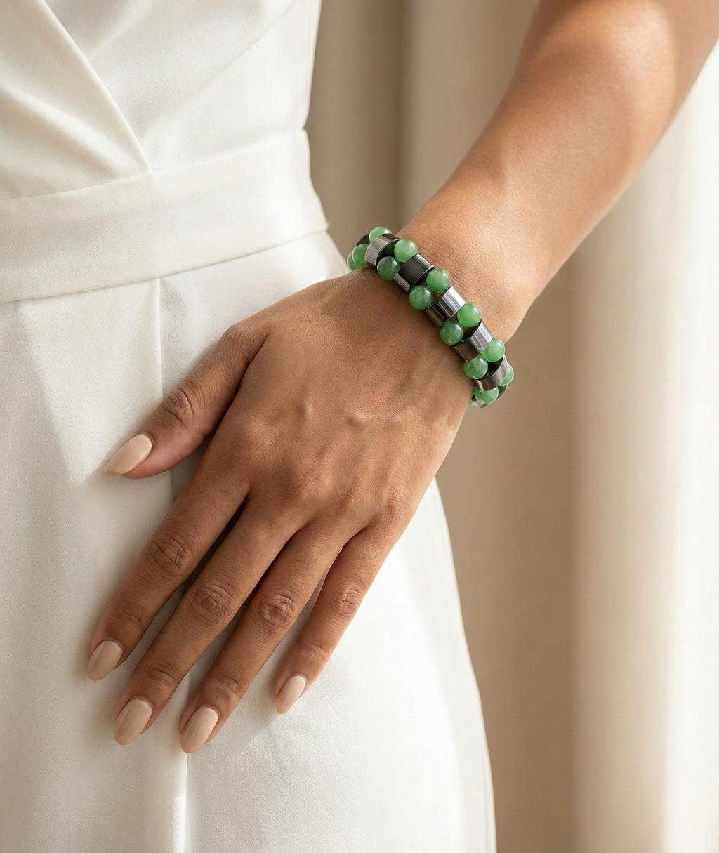 Hand wearing a green beaded bracelet on a plain background