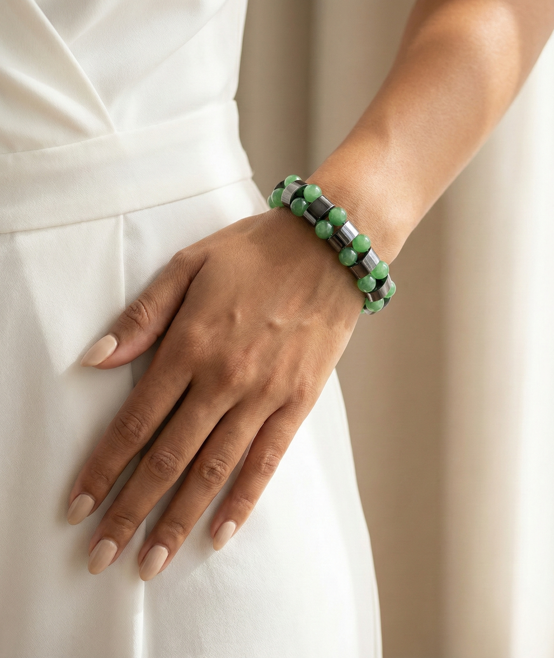 Hand wearing a green beaded bracelet on a plain background